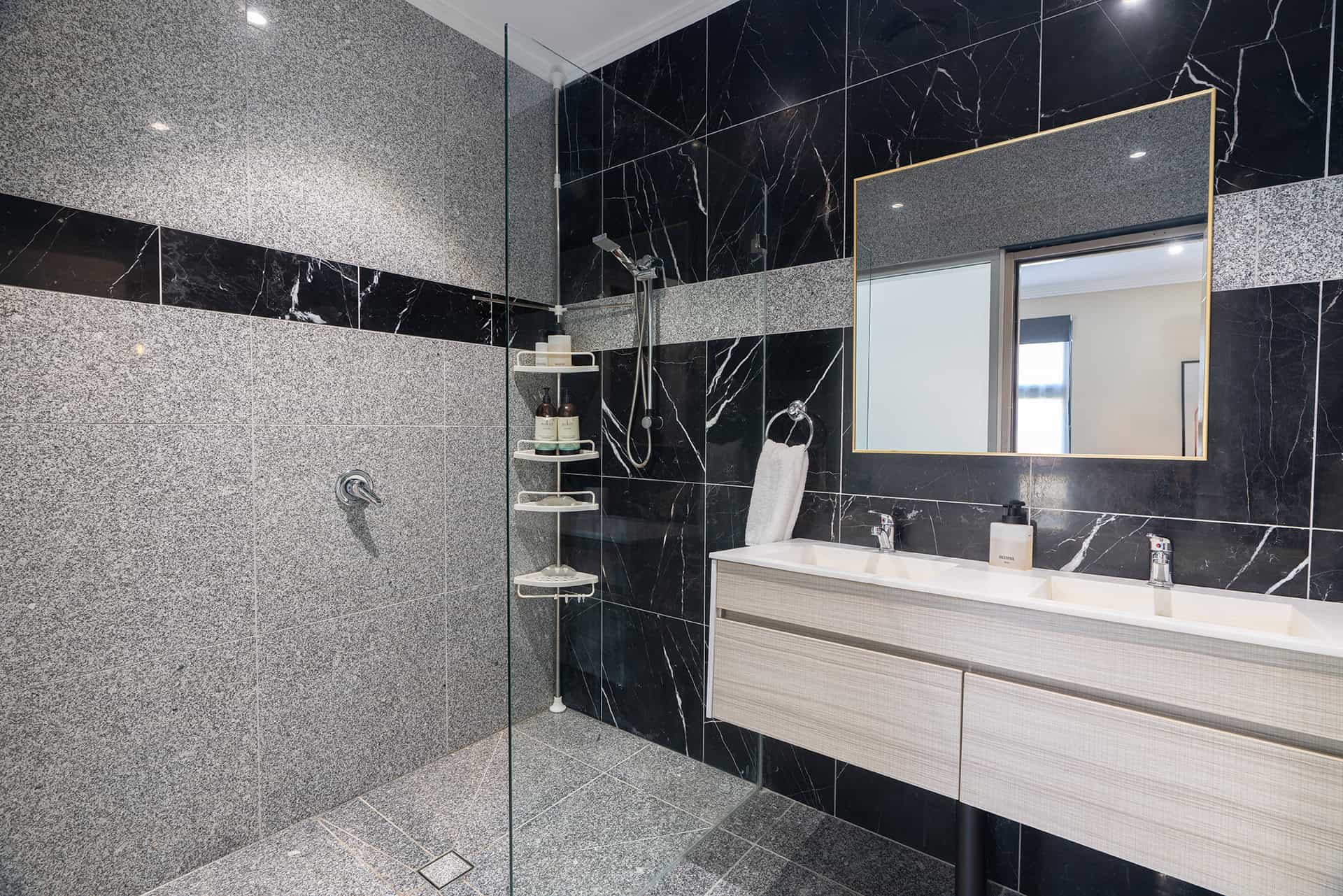 Home 4 Luxurious black and grey tiled bathroom featuring a double sink vanity, modern mirror, and elegant shower area.
