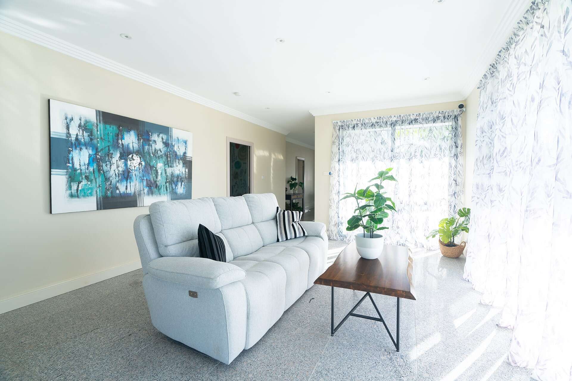 Home 6 Clean, bright living space featuring a white sofa, potted plants, and large windows with patterned curtains for a welcoming vibe.