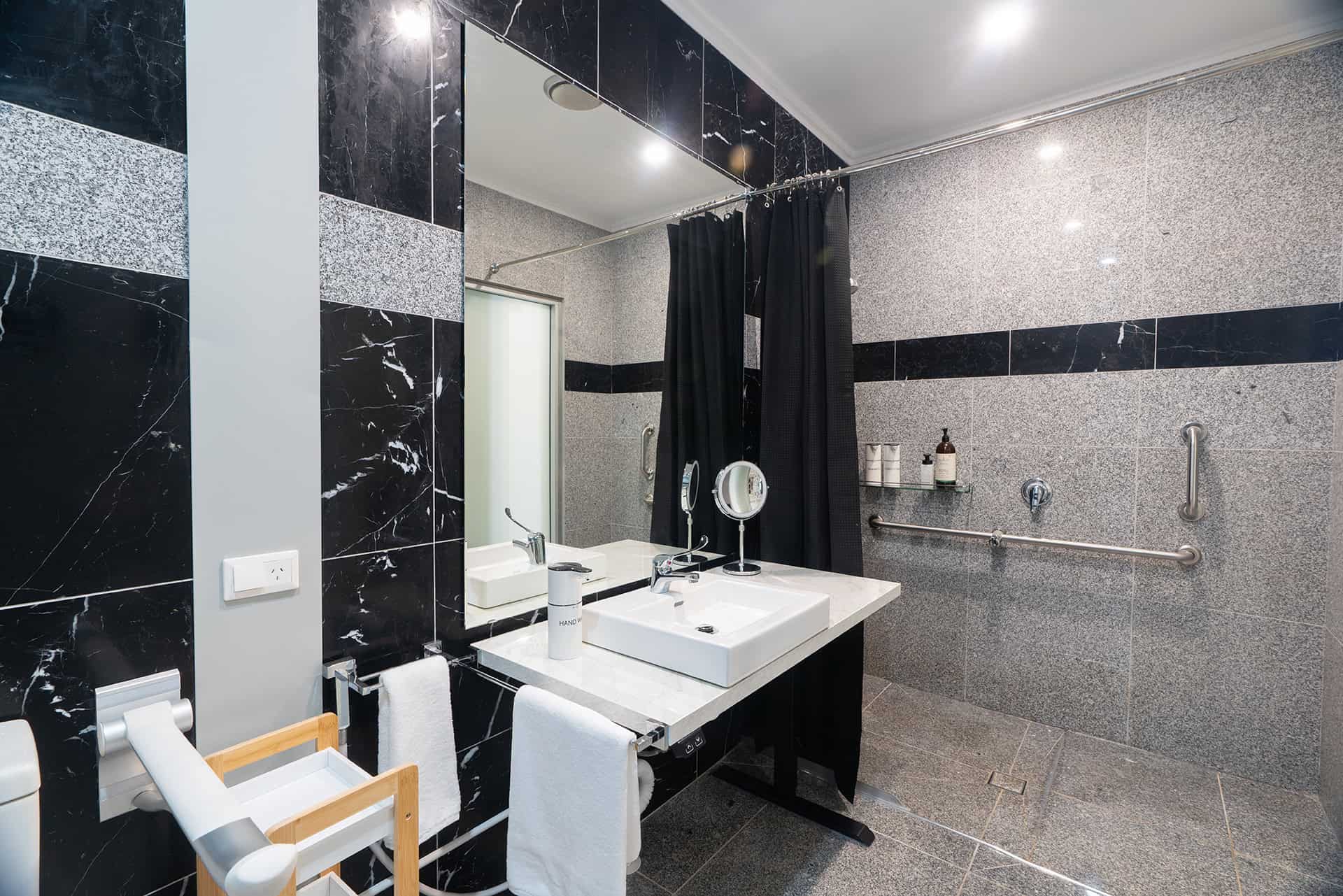 Home 15 Bright, stylish bathroom featuring black marble tile, accessible grab bars, and contemporary amenities.