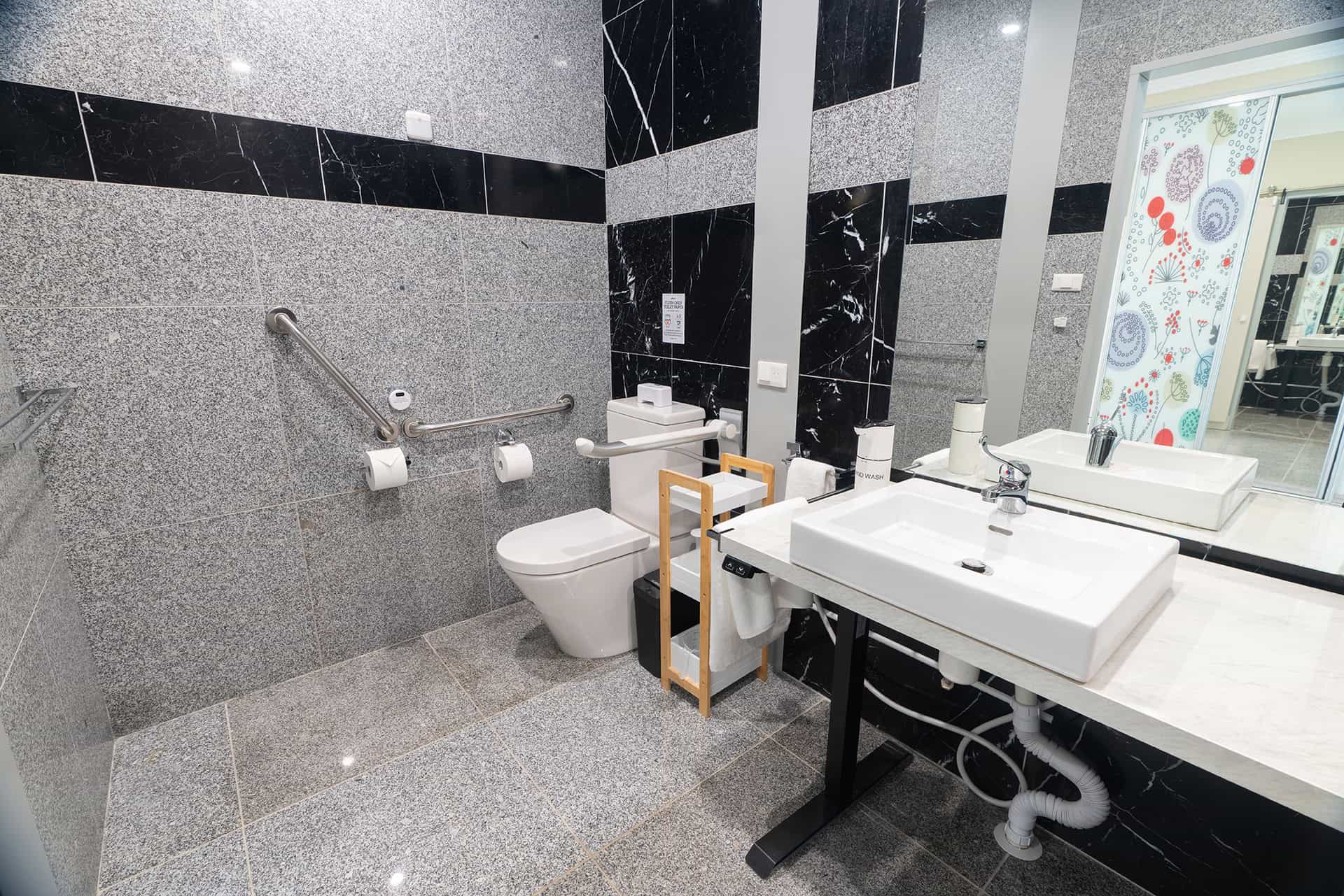 Home 16 Accessible bathroom featuring grab bars, raised toilet, and stylish black and grey tile design.